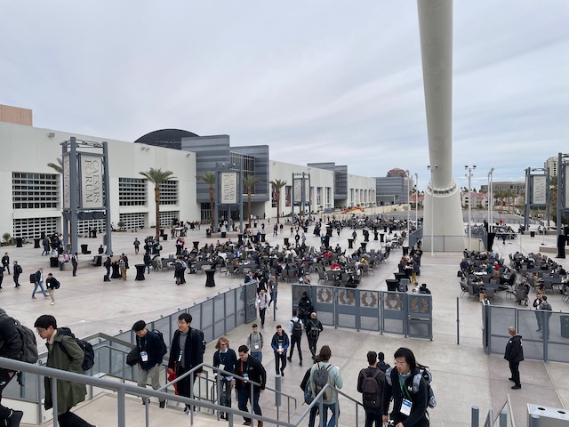 A view of a large plaza with tables, chairs, and hundreds of people walking or sitting.