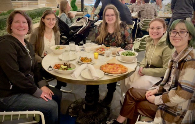 Five women sit around a table with dinner